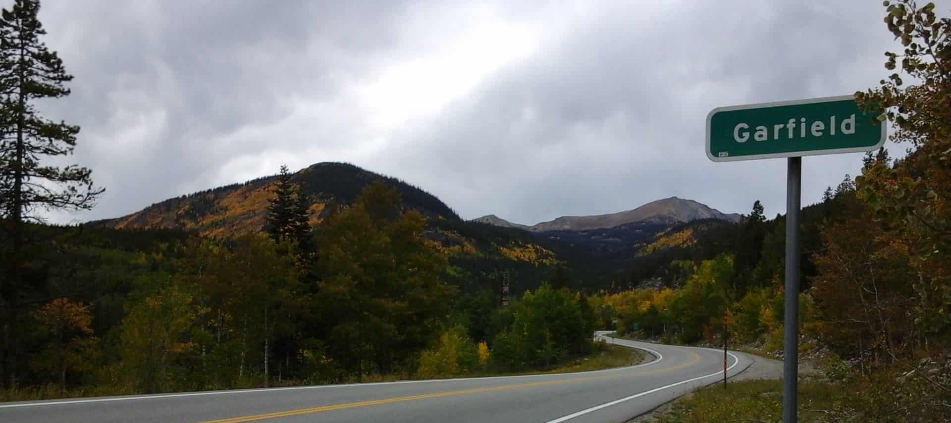 Green Garfield sign next to a highway winding through the mountains covered in trees with green and orange leaves