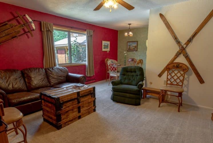 Living room with red, green, and cream walls, carpeting, brown leather couch, green arm chair, wooden trunk, and wooden hutch