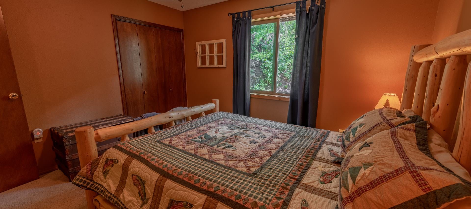 Bedroom with brown walls, carpeting, wooden log bed, homemade quilt, and large trunk