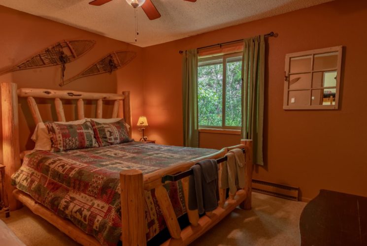 Bedroom with brown walls, carpeting, wooden log bed, homemade quilt, and wooden nightstands