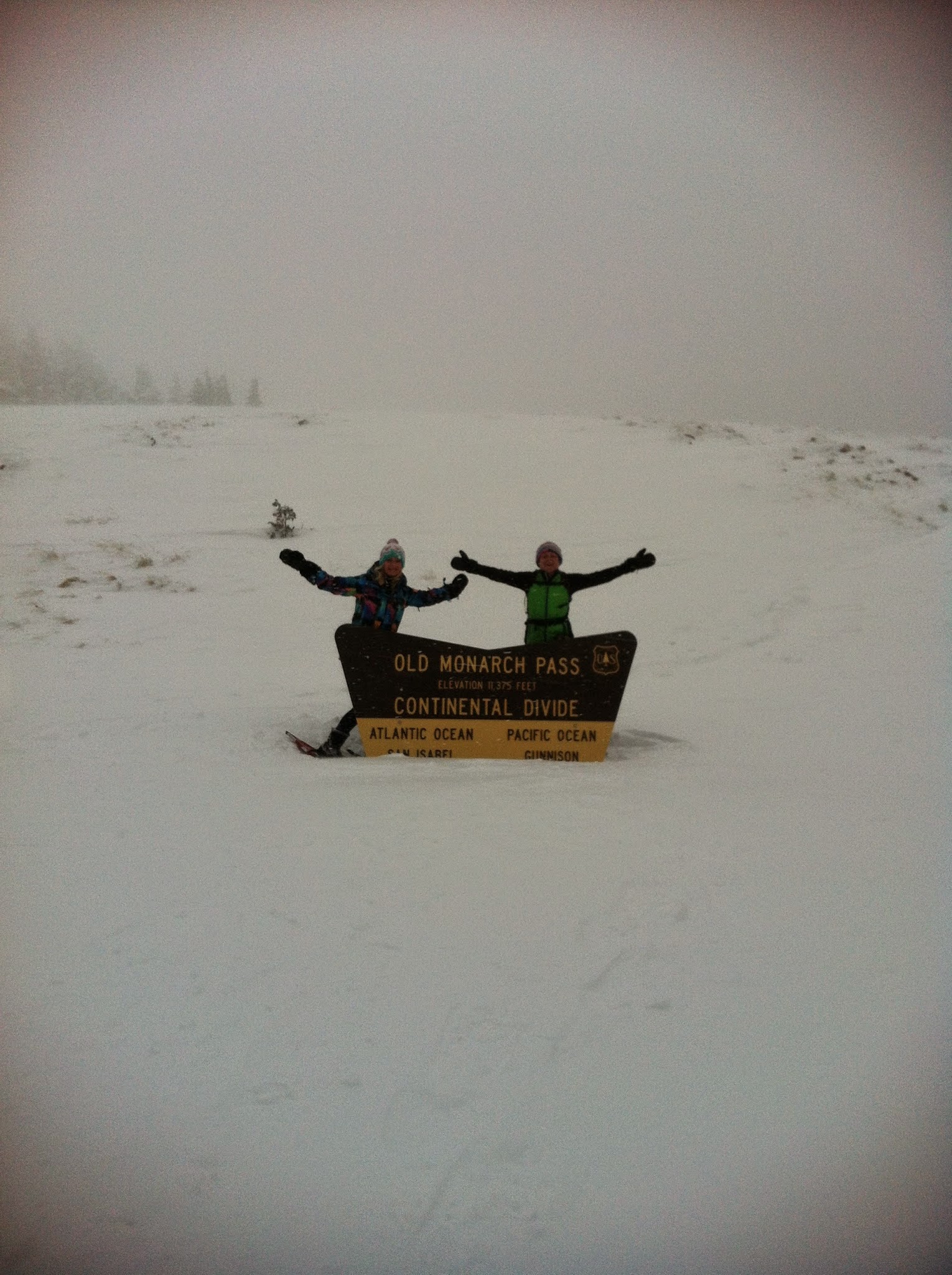Two ladies snowshoeing at the top of Old Monarch Pass around the Continental Divide sign.