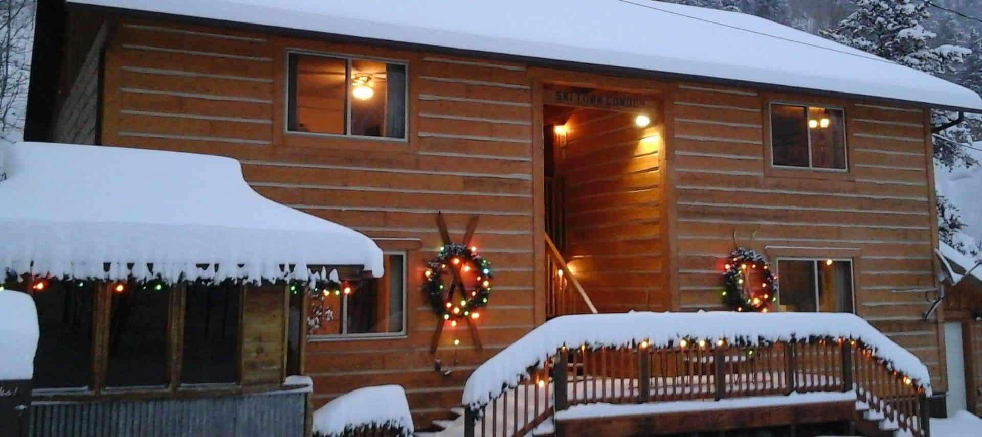 Exterior view of the property with wooden siding all covered in snow and decorated with lights and wreaths