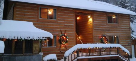 Exterior view of the property with wooden siding all covered in snow and decorated with lights and wreaths