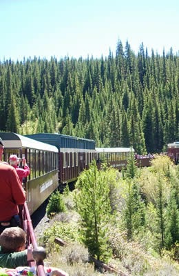 Passenger train ride along a mountain curve, with passengers taking photos and kids look out at the forest.