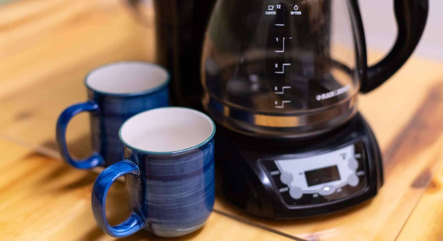 Close up view of two blue coffee mugs next to a coffee pot on a wooden counter
