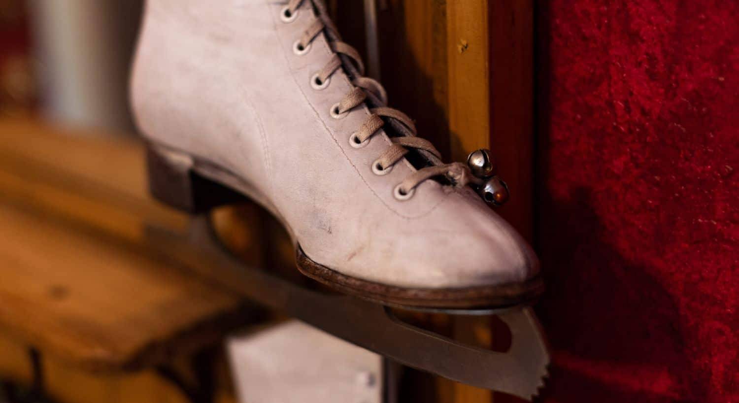 Antique white ice skate with a bell hanging off the wall.