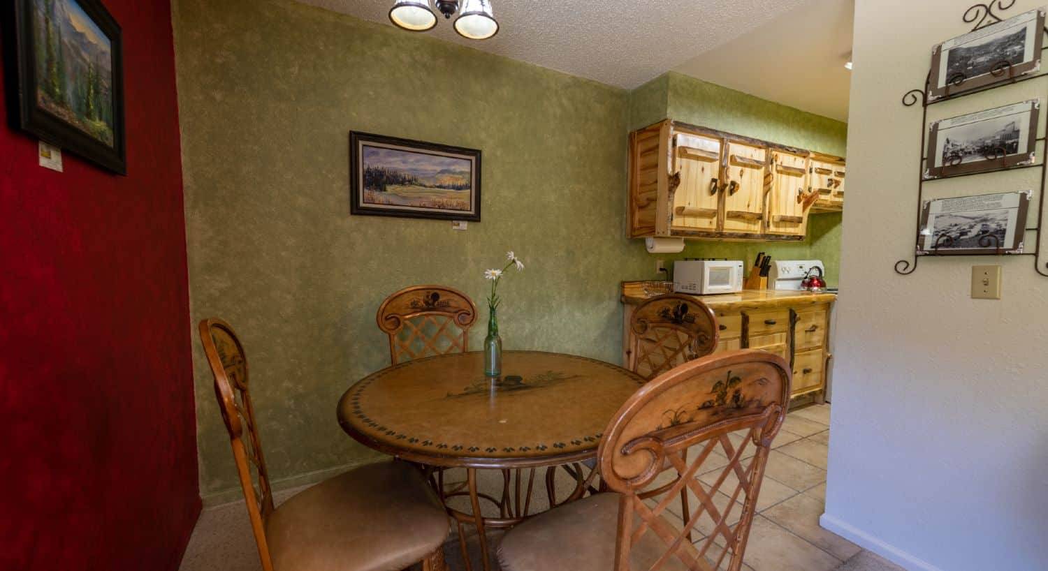 Charming round dining table with four chairs, kitchen to the right with rustic log cabinets.