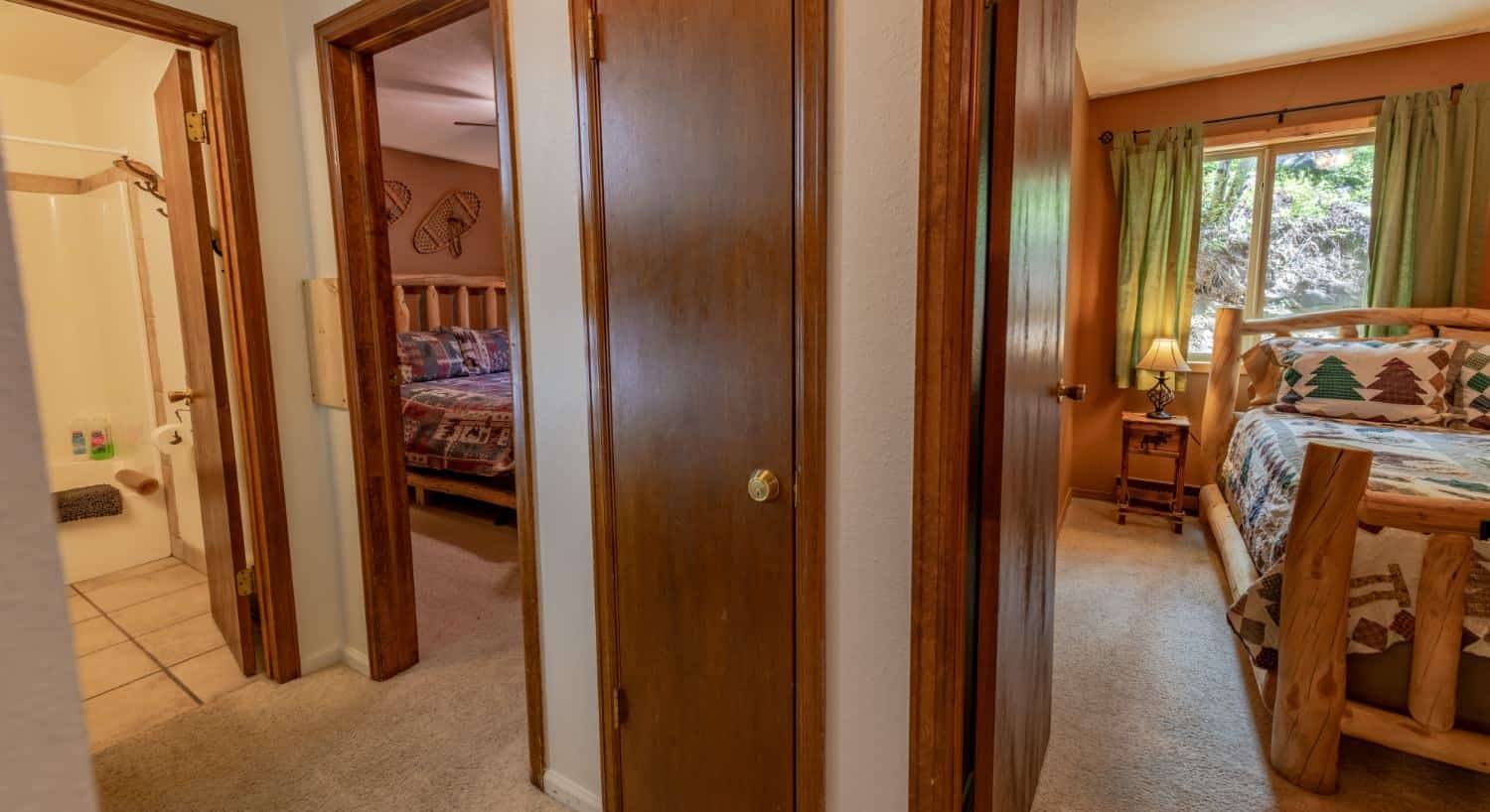 Hallway with cream walls, carpeting, and views into two bedrooms and a bathroom