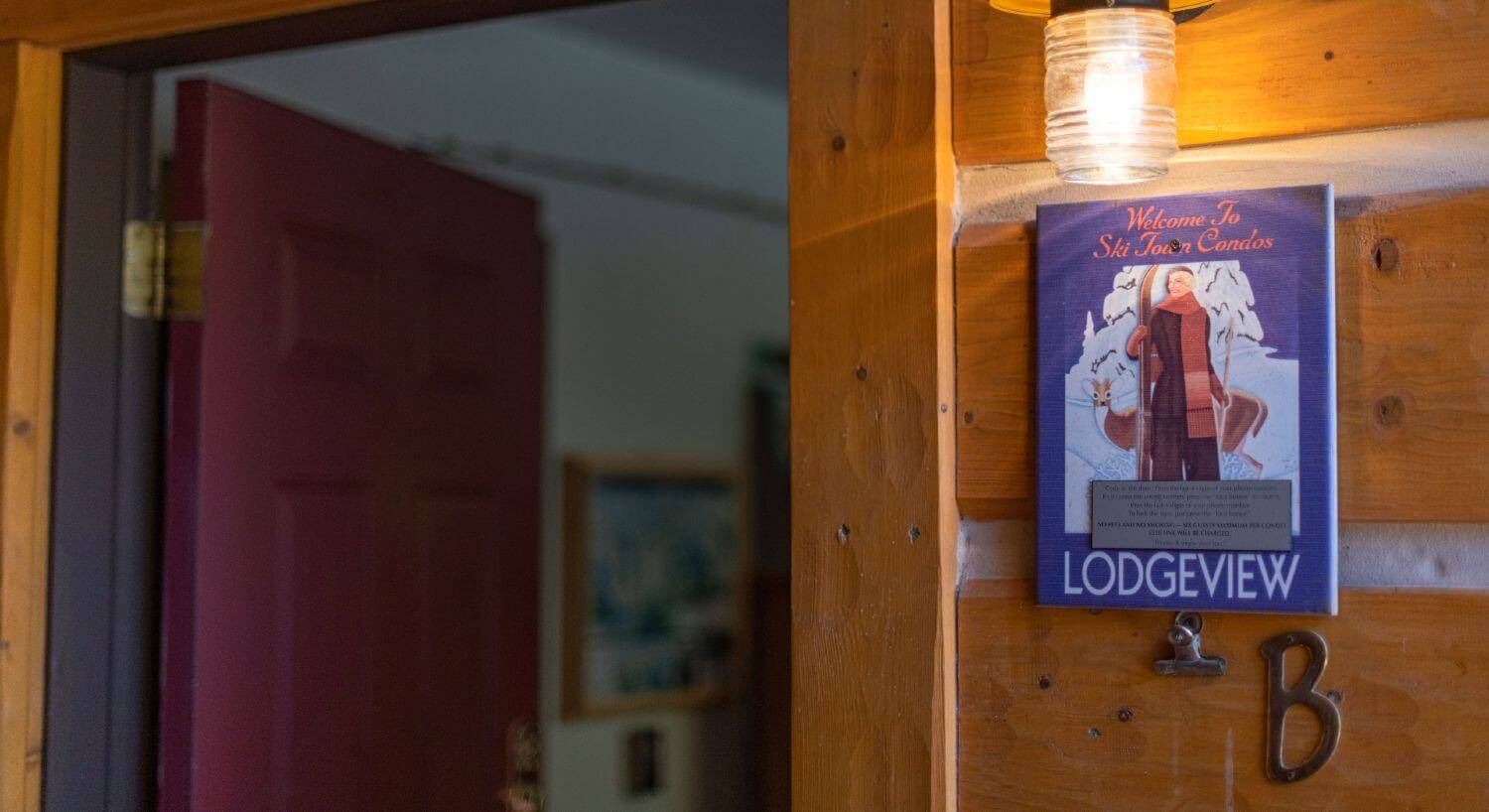 Entrance to Condo B with outdoor light shining on the entrance sign, and log siding.