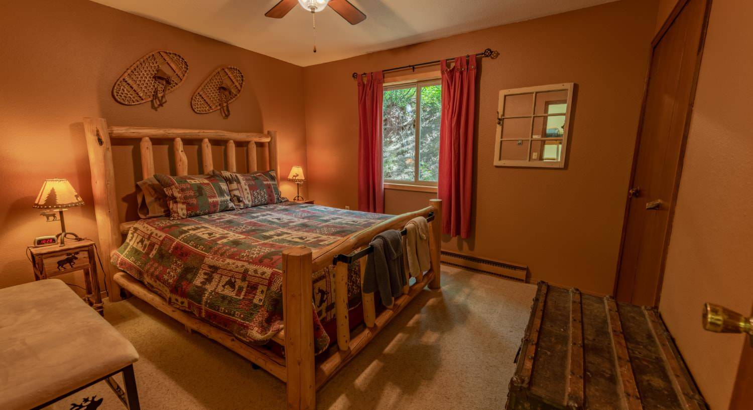 Bedroom with brown walls, carpeting, wooden log bed, homemade quilt, and large trunk