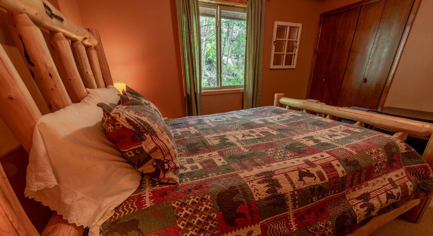Guest bedroom with a queen size log bed, lodge style quilt, and brown walls.