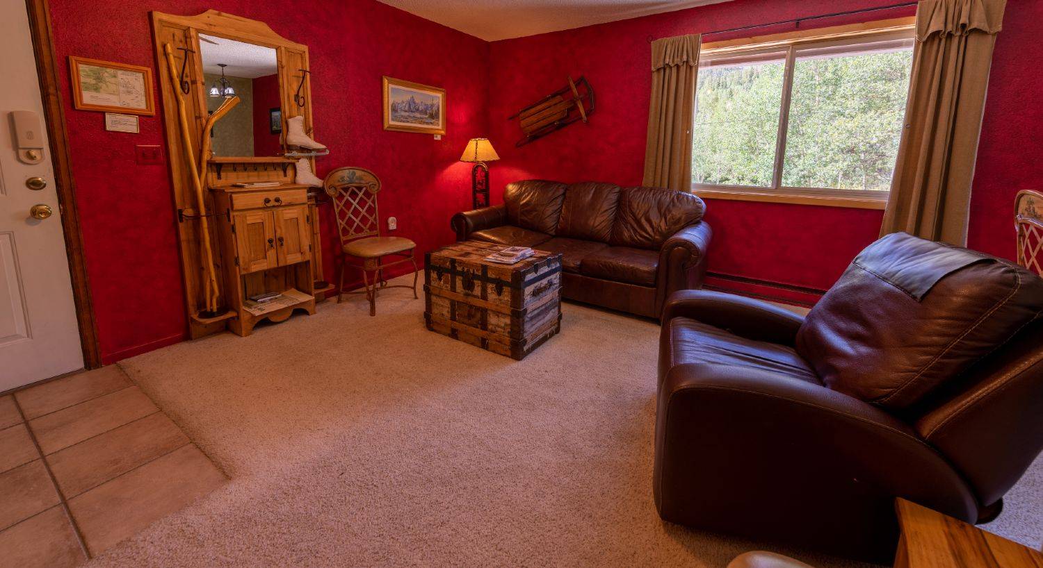 Condo C living room with a brown leather sofa, antique trunk, two chairs, painting on the wall, mirror armoire next to the door.