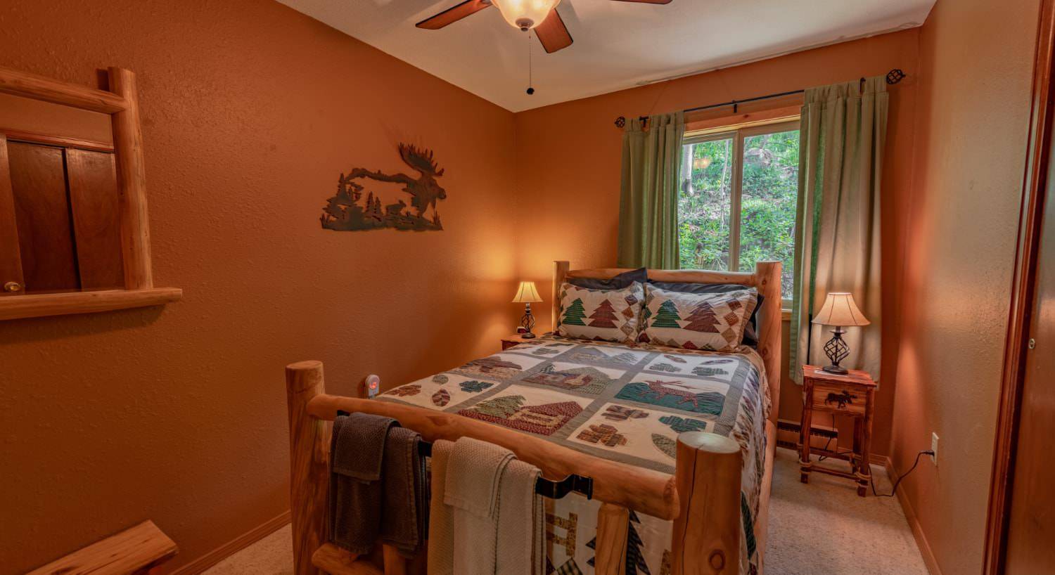 Bedroom with brown walls, carpeting, wooden log bed, homemade quilt, and wooden nightstands