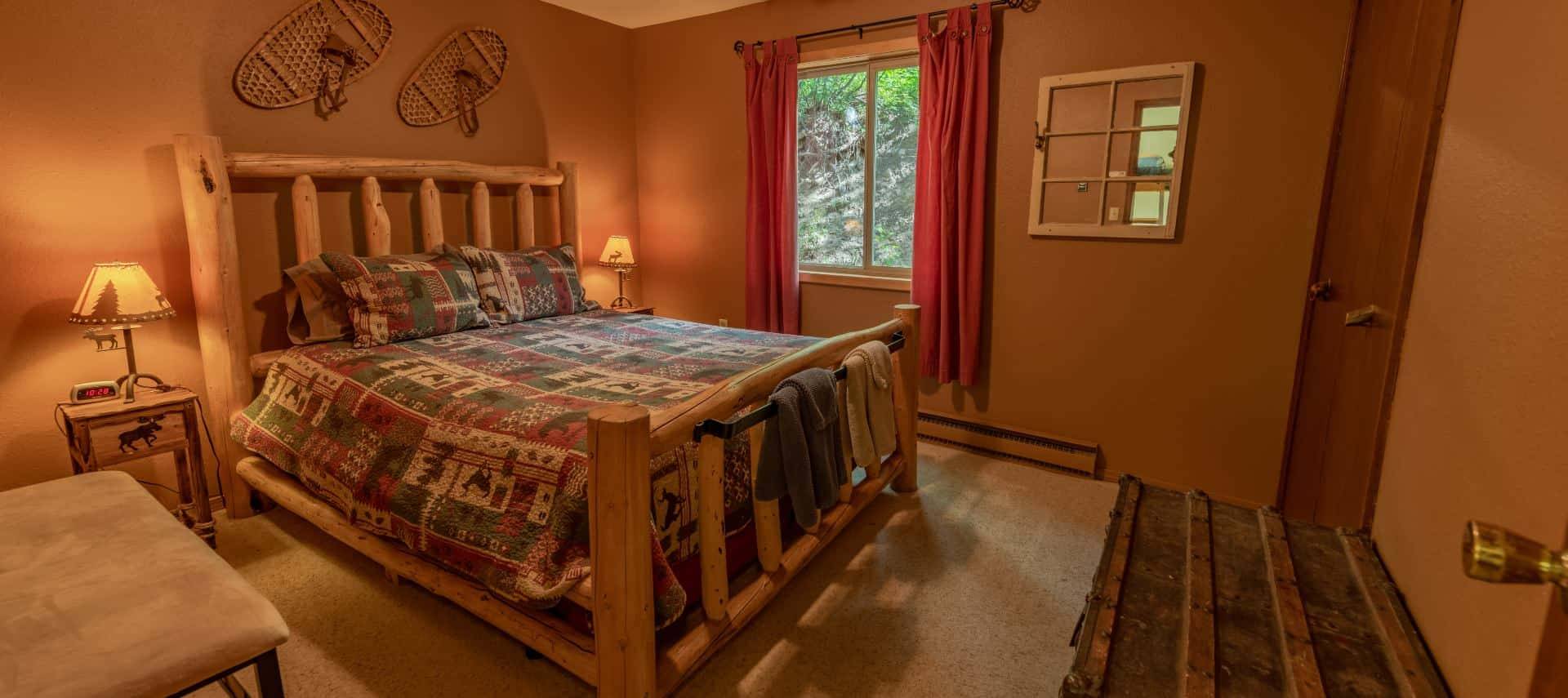 Bedroom with brown walls, carpeting, wooden log bed, homemade quilt, and large trunk